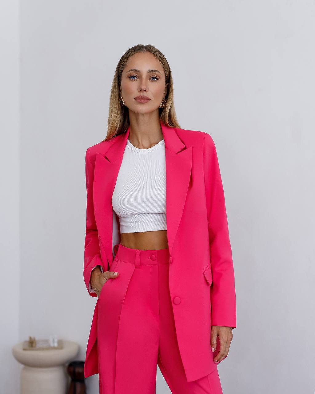 Woman wearing a bright pink suit with a white top against a plain background