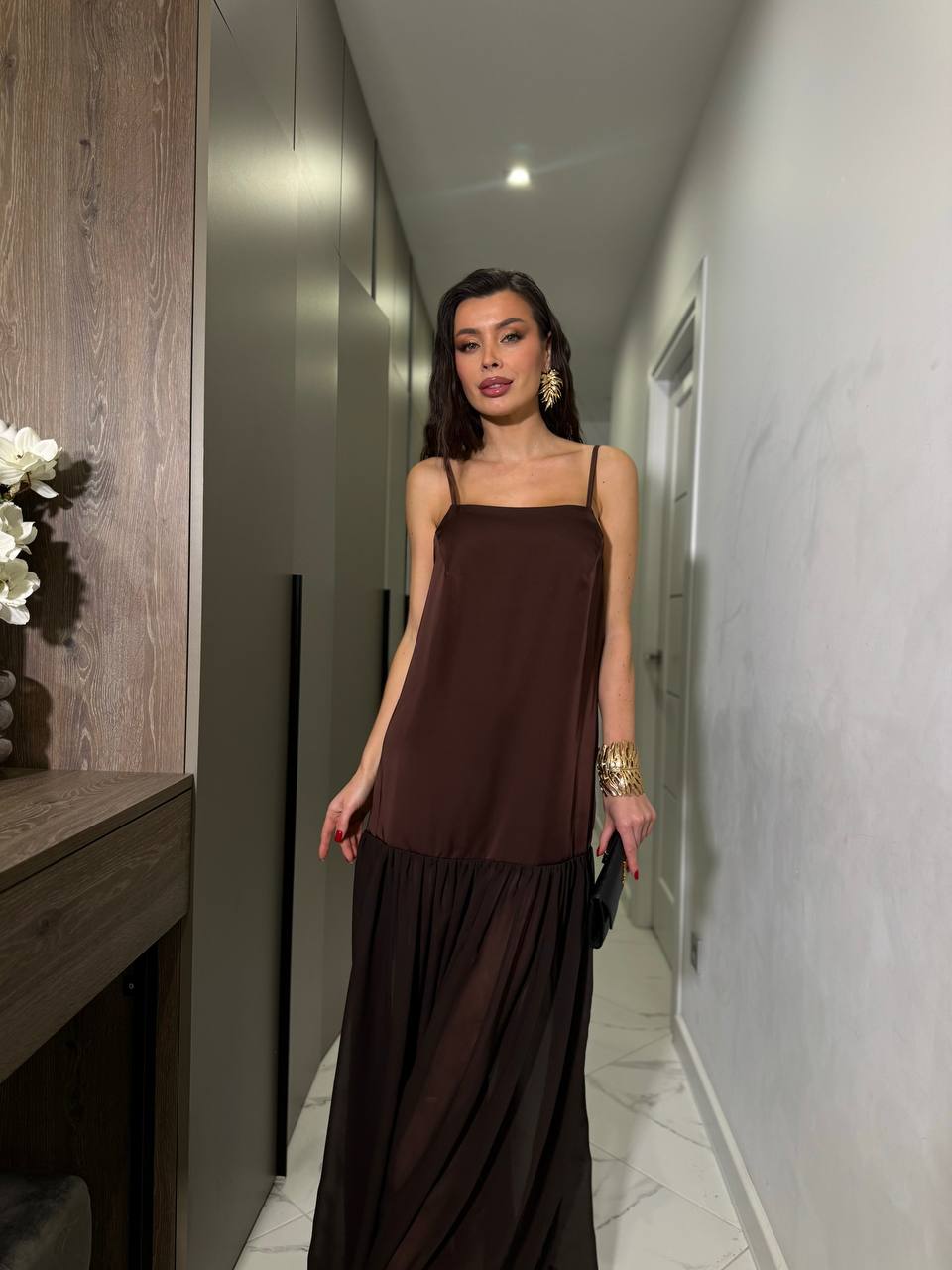 Woman in a brown dress standing in a hallway with a neutral background