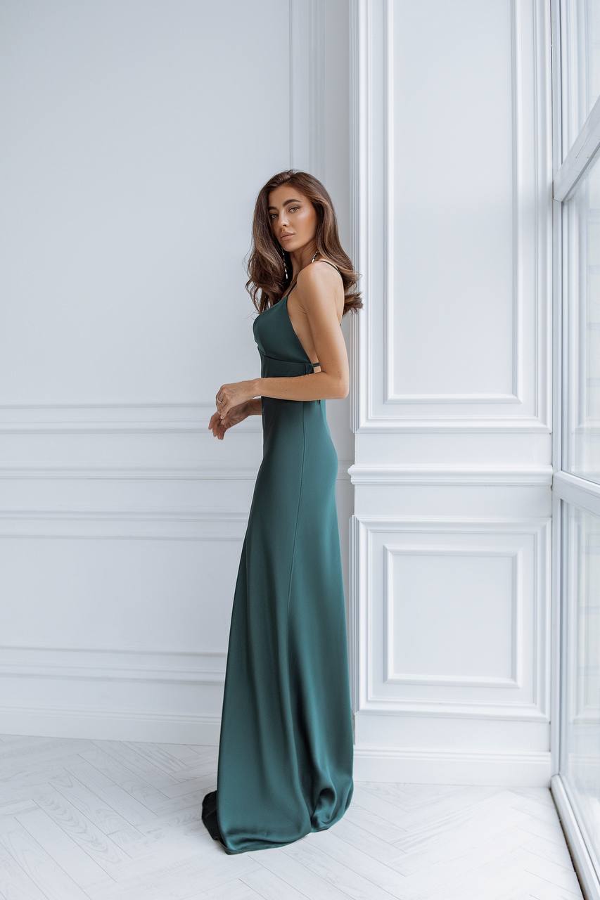 Woman in a long teal dress standing against a white paneled wall.