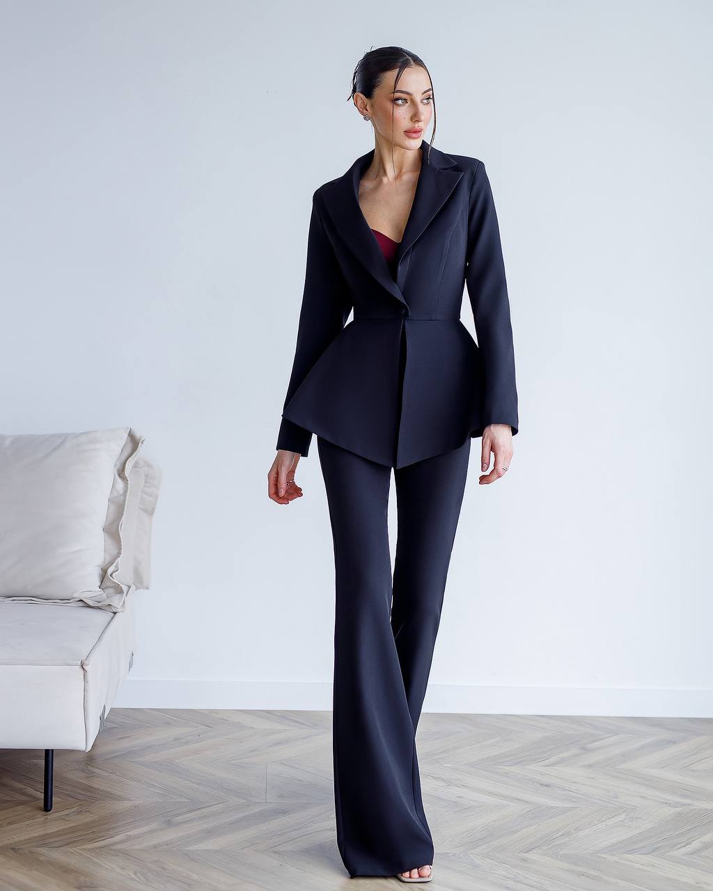 Woman wearing a dark blue suit standing in a minimalistic room with a white couch.