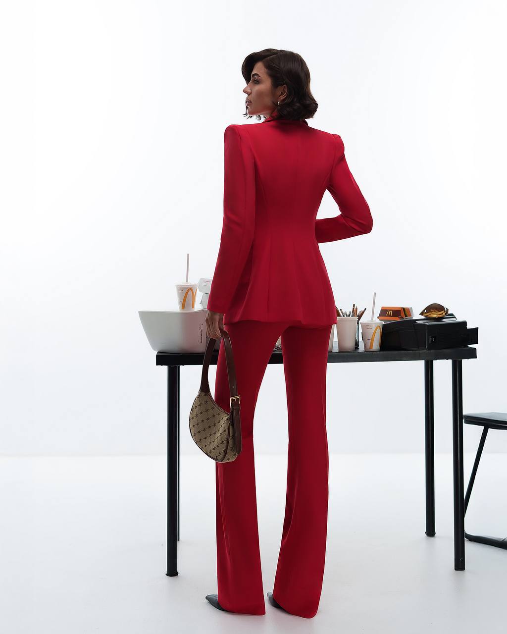 Woman in a red suit standing in front of a table with various items on a white background