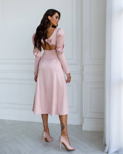 Woman wearing a pink dress with long sleeves and a fitted skirt against a white wall.