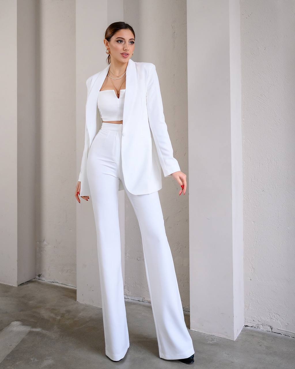 Woman wearing a white suit standing against a plain wall.