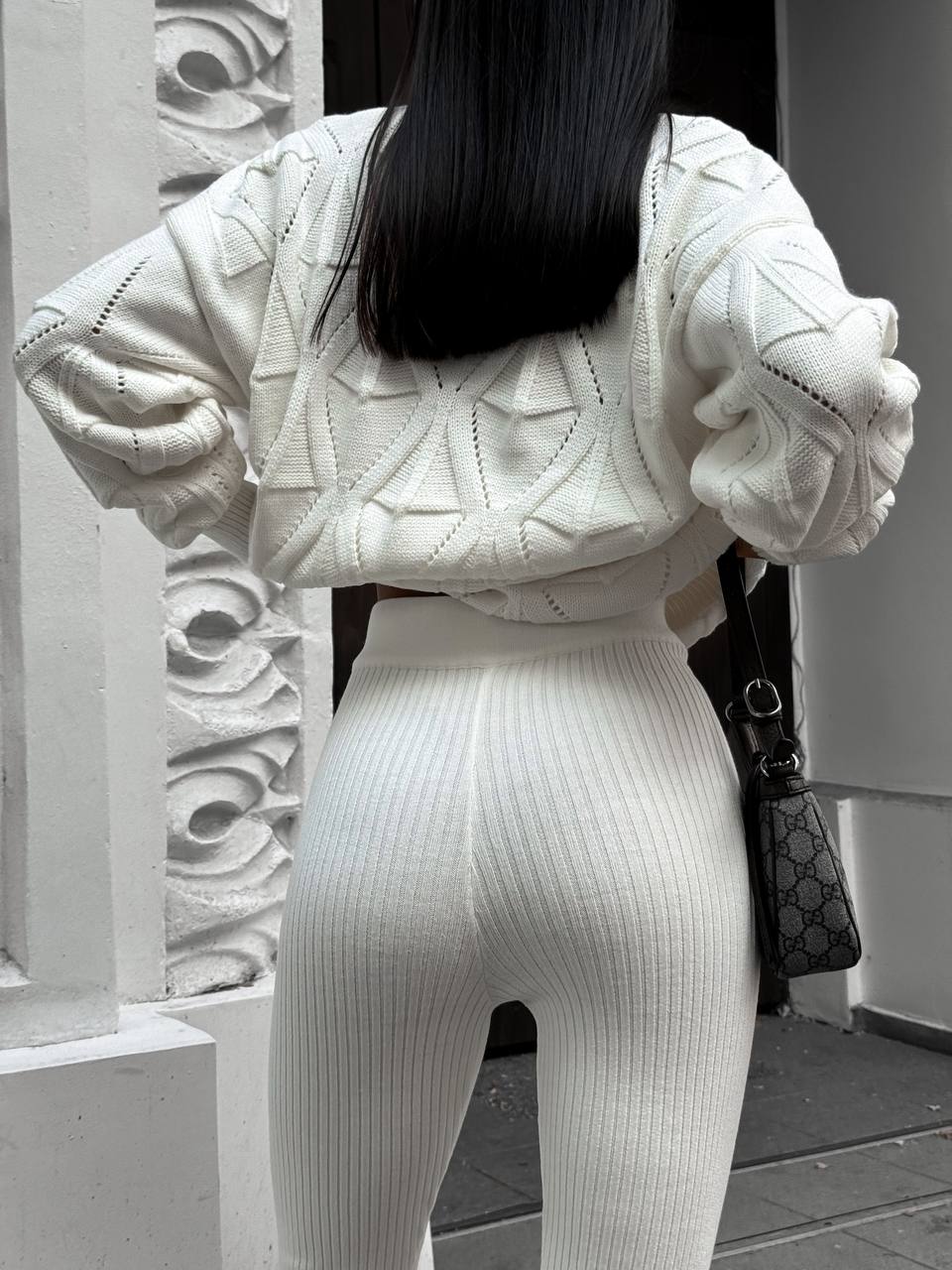 Person wearing a white knit outfit with a textured pattern, holding a Gucci handbag.