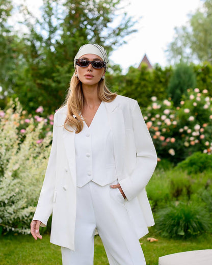 Woman in a white outfit standing in a garden with greenery and flowers in the background
