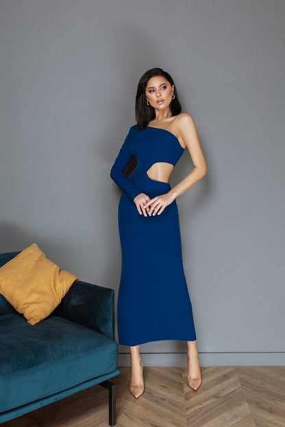 Woman in a blue dress standing in a room with a gray wall and a blue couch.