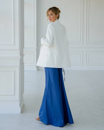 Woman wearing a white coat over a blue dress in a room with white walls.