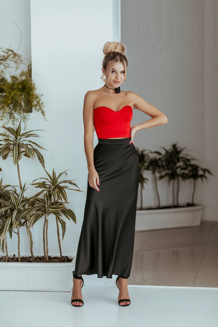 Woman in a red top and black skirt standing indoors with plants in the background
