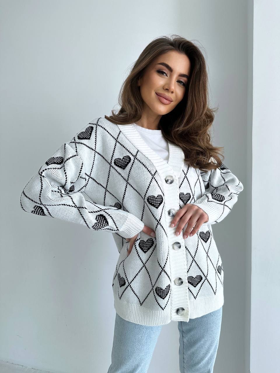 Woman wearing a white cardigan with black heart patterns on a plain background