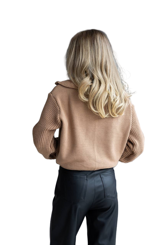 Person wearing a beige sweater and dark pants on a white background