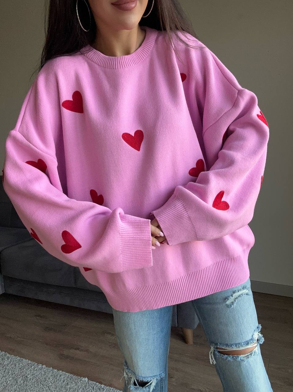 Person wearing a pink sweater with red heart patterns in a casual setting.