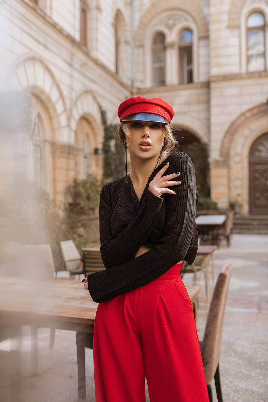 Woman in black top and red pants with a red cap in an outdoor setting with architectural background