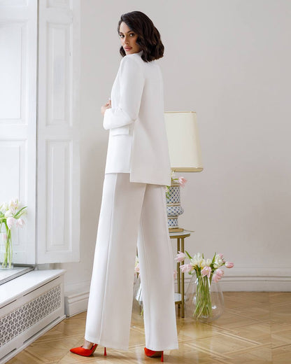 Woman in a white suit standing in a room with flowers and a lamp.