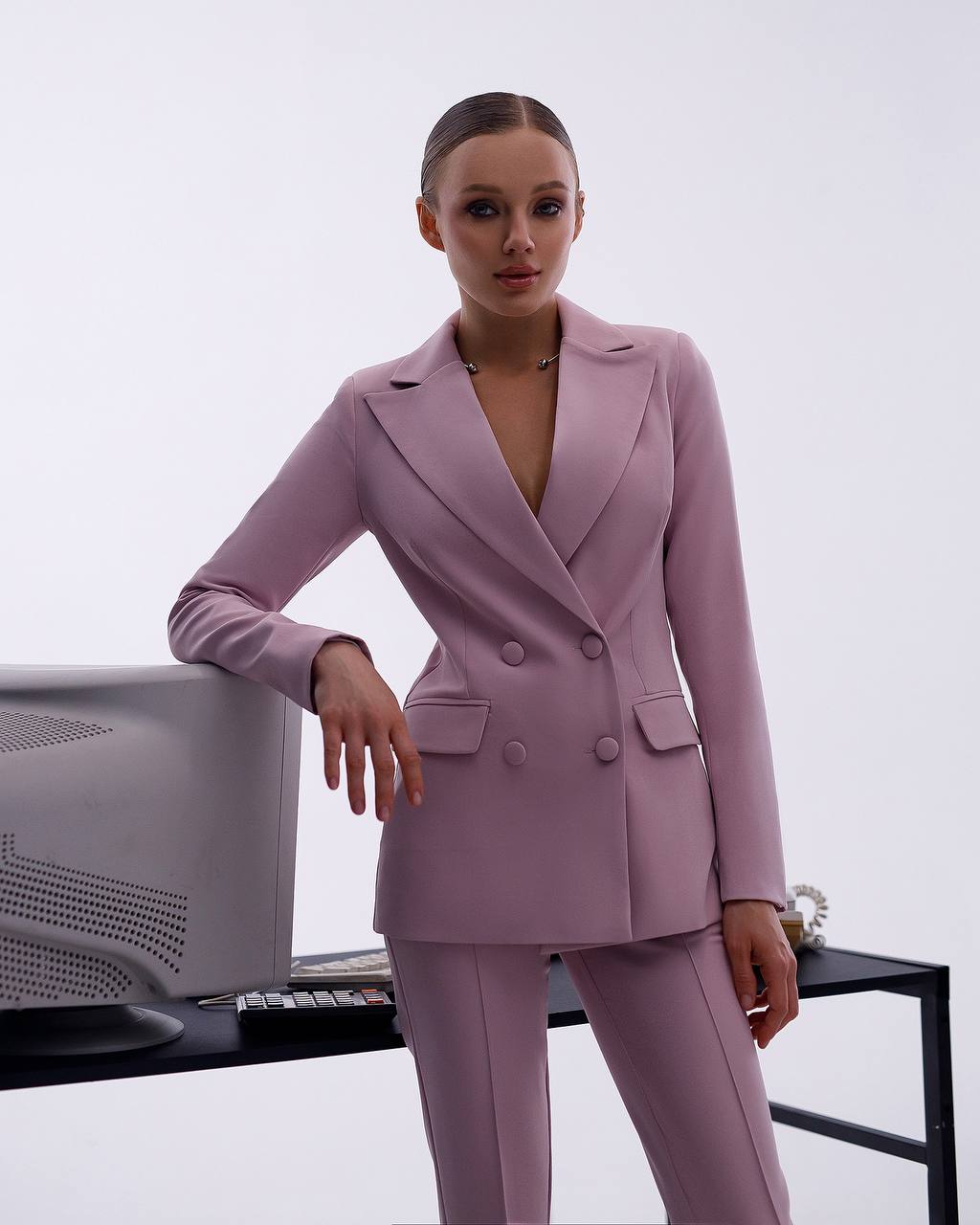 Woman in a lavender suit standing next to a computer monitor on a white background