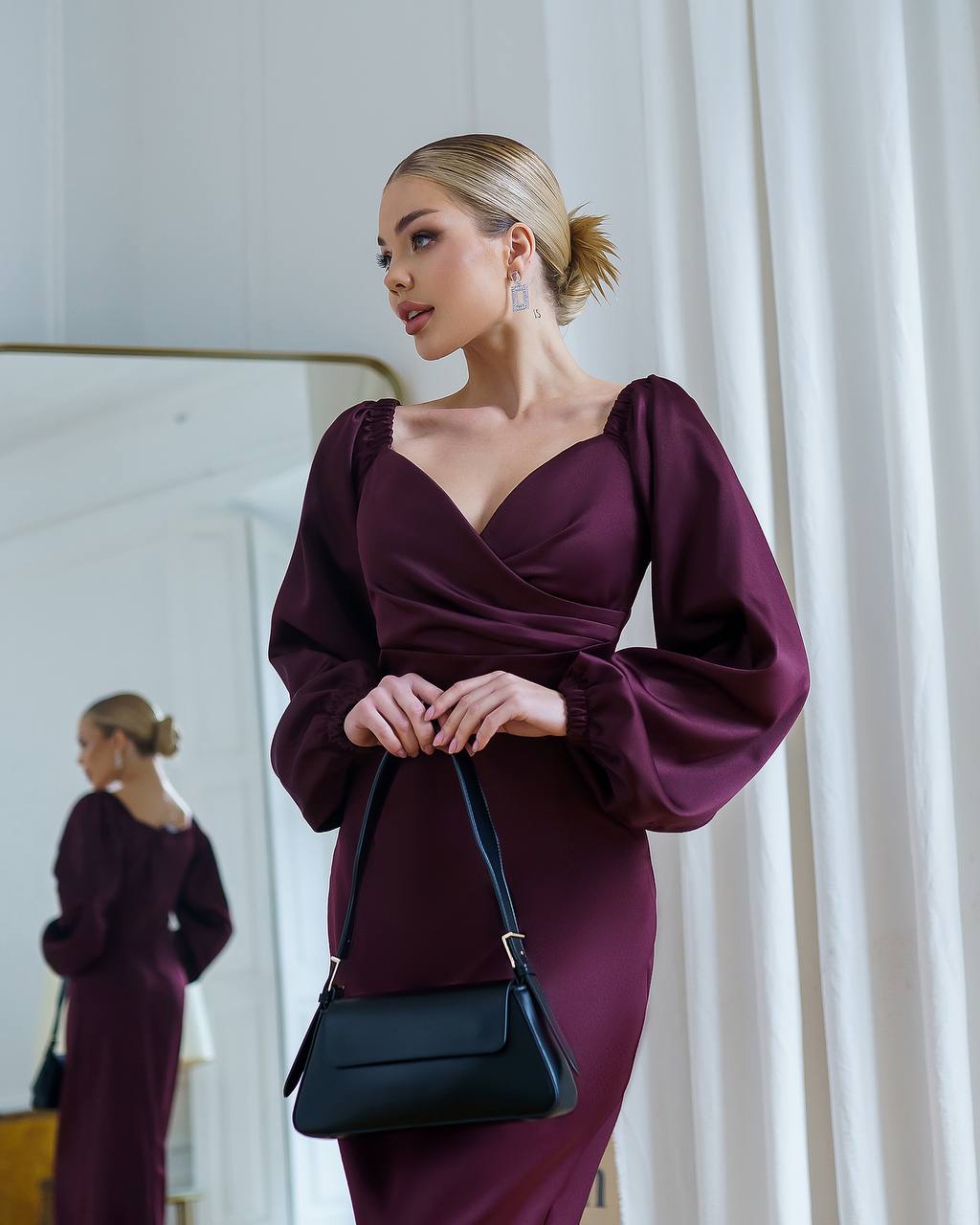 Woman in a burgundy dress holding a black handbag in front of a mirror.