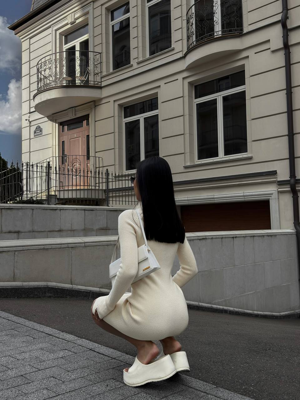 Woman in a white outfit squatting in front of a building