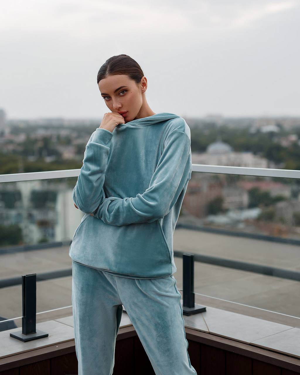 Person wearing a blue tracksuit on a balcony with a cityscape background