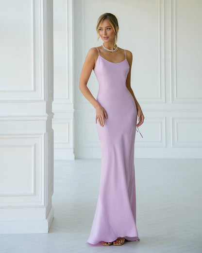 Woman wearing a long lilac dress against a white wall