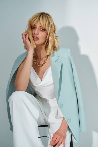 Woman wearing a light blue blazer over a white outfit with a plain background