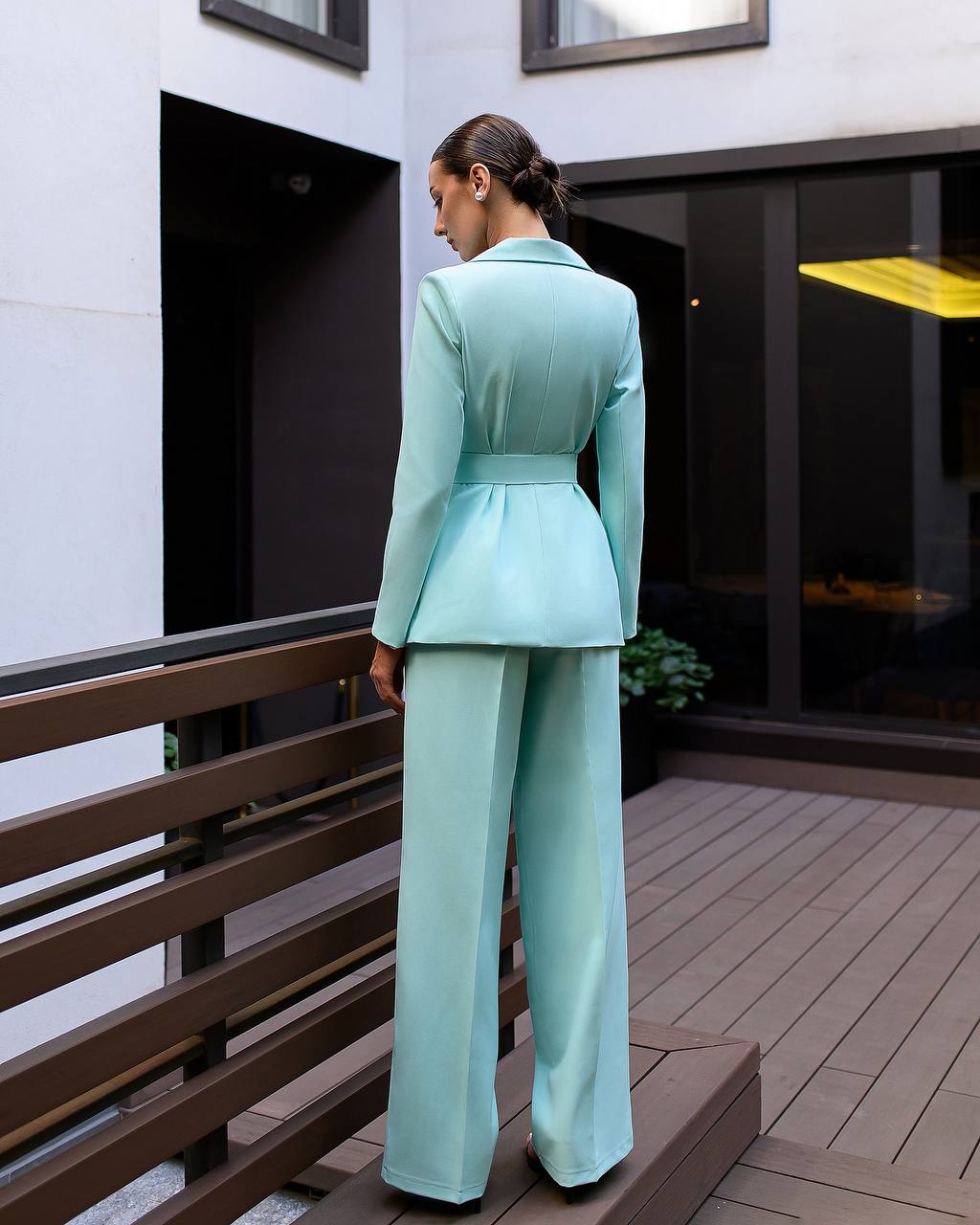 Woman in a light blue suit standing on a wooden deck.