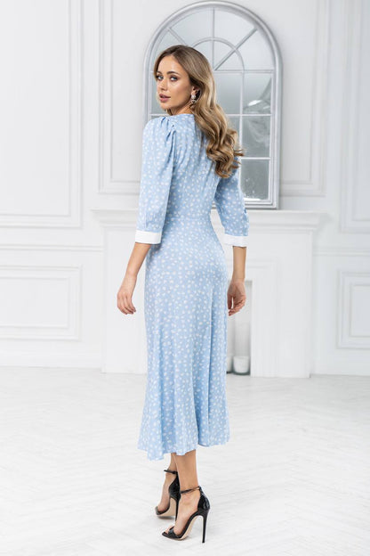 Woman wearing a light blue dress with a white pattern in a bright room.