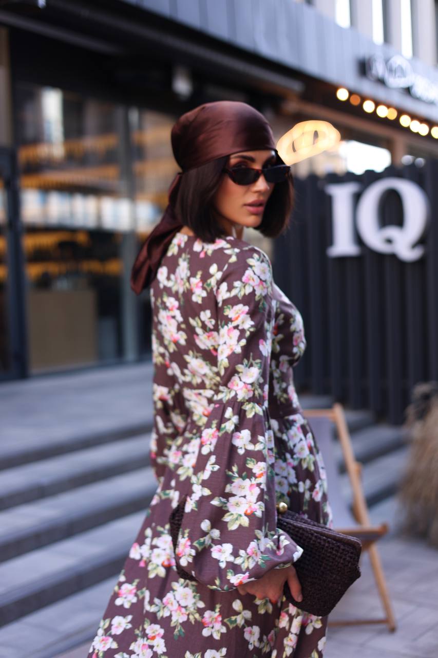 Woman in a floral dress and hat walking outdoors with a blurred background