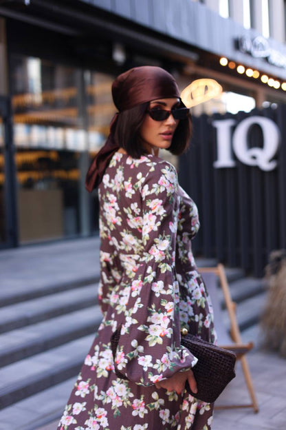 Woman in a floral dress and hat walking outdoors with a blurred background