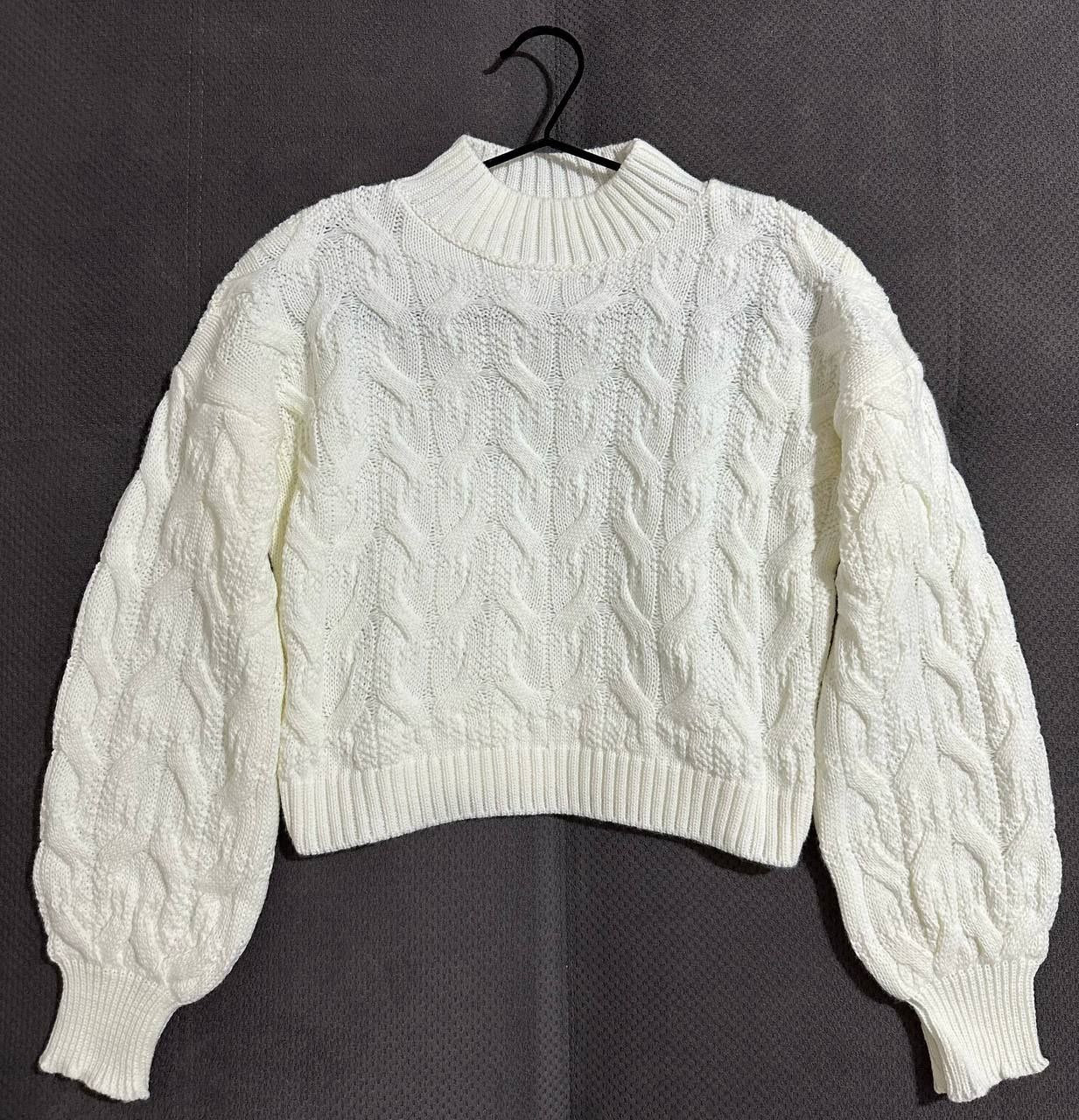 White cable knit sweater on a black hanger against a dark background