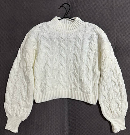White cable knit sweater on a black hanger against a dark background