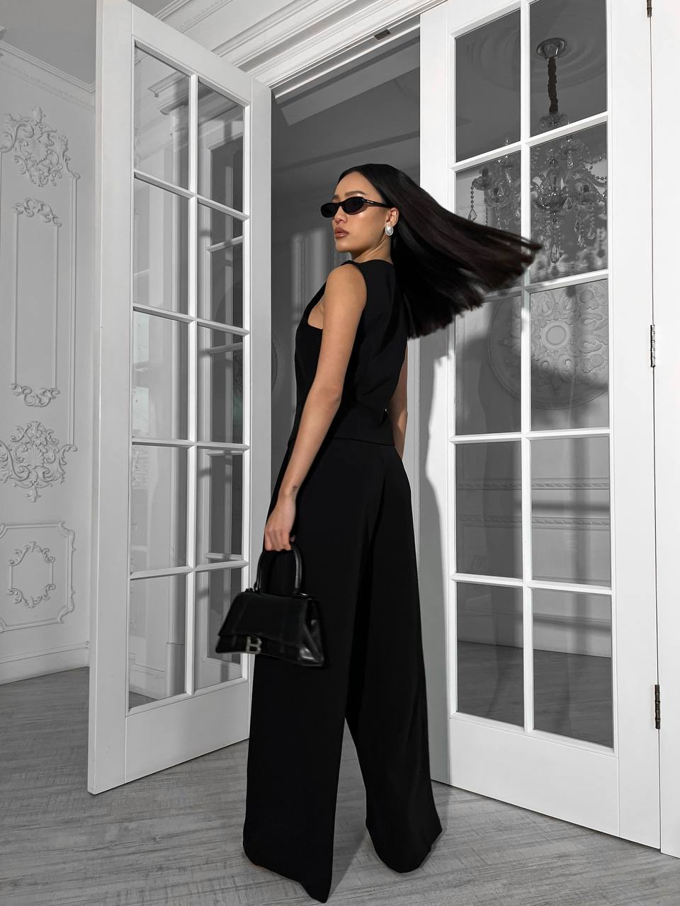 Woman in a black outfit standing in a room with white walls and glass doors.
