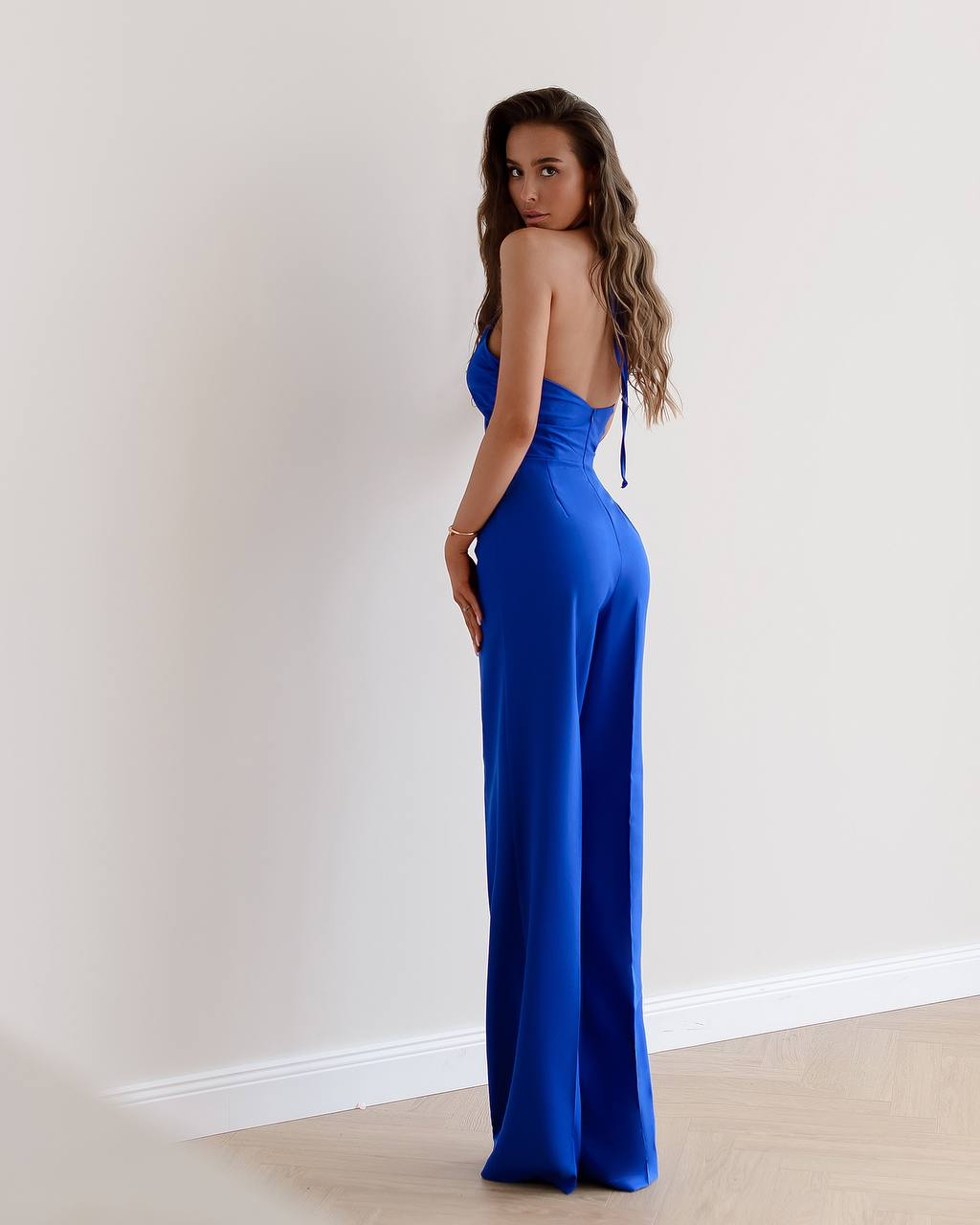Woman wearing a blue evening gown against a plain wall.