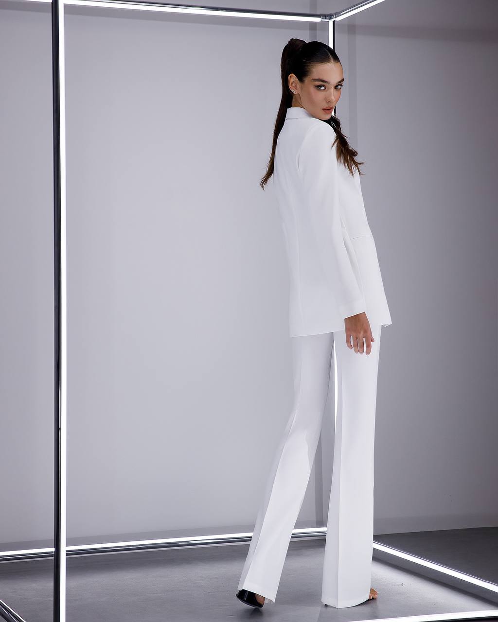 Woman wearing a white suit standing in a futuristic, metallic room.