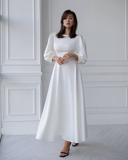 Woman wearing a white dress standing against a white wall.