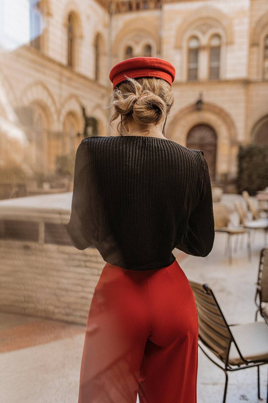 Person wearing a red hat and red pants standing in front of a historic building.