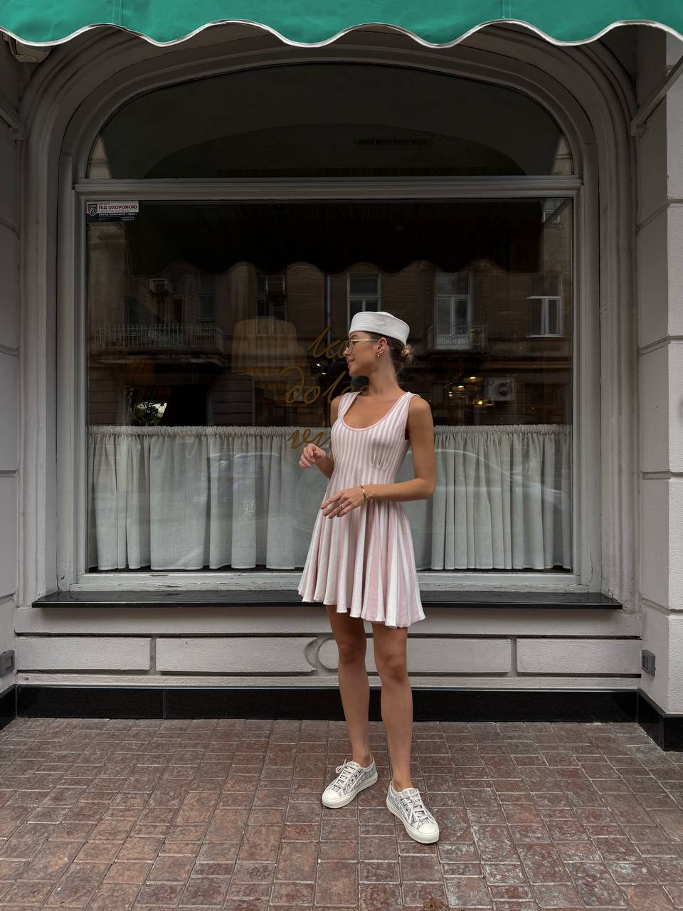 Woman in a white dress and cap standing in front of a store with a green awning.
