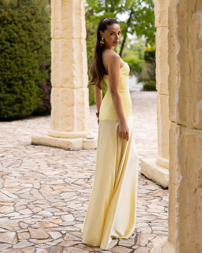 Woman in a yellow dress standing in an outdoor setting with stone pathways and greenery.