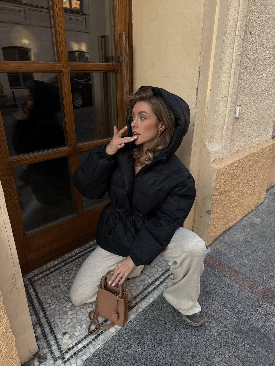 Woman in a black coat sitting on a step next to a building entrance.