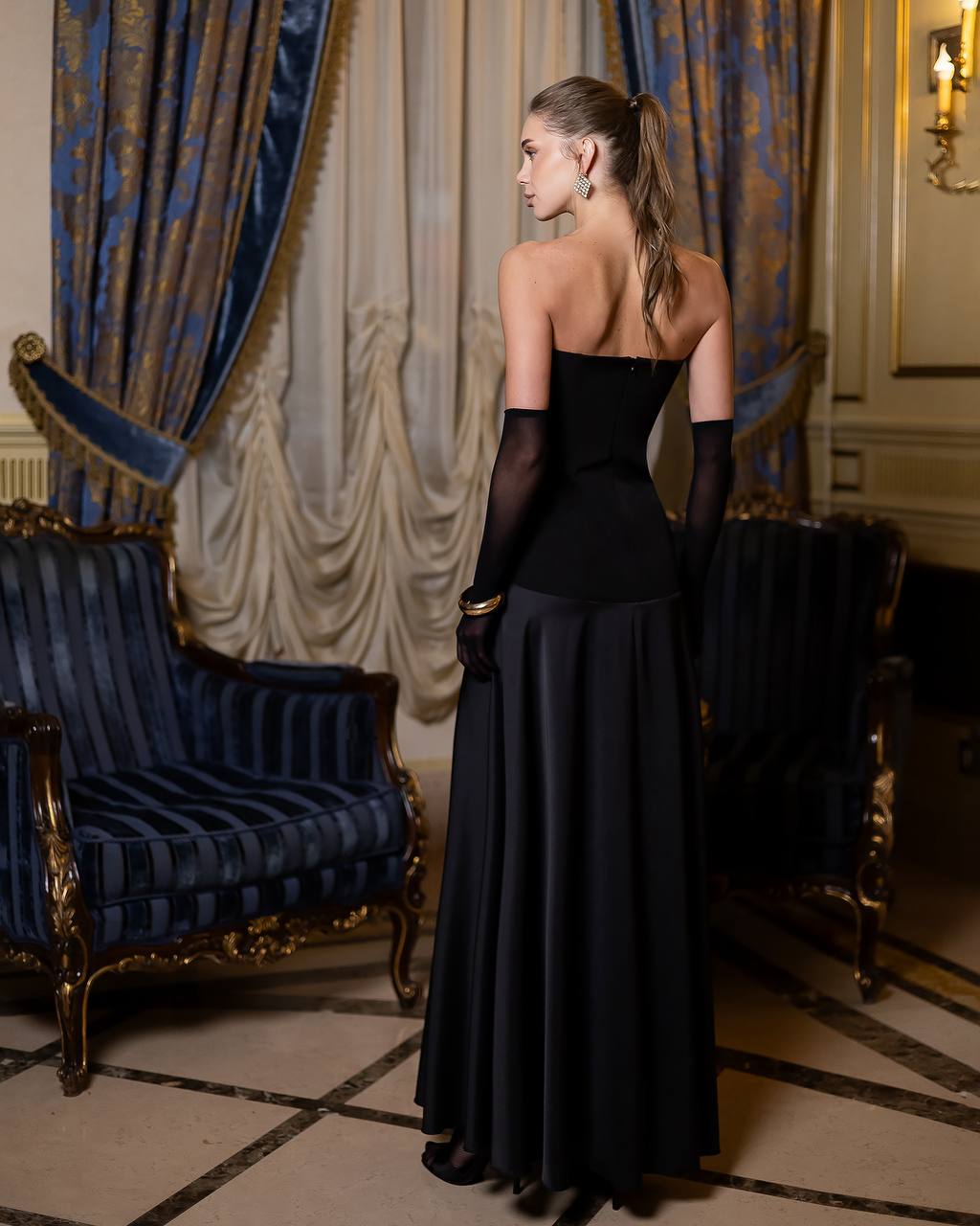 Woman in a black evening gown standing in an elegant room with blue and gold decor.