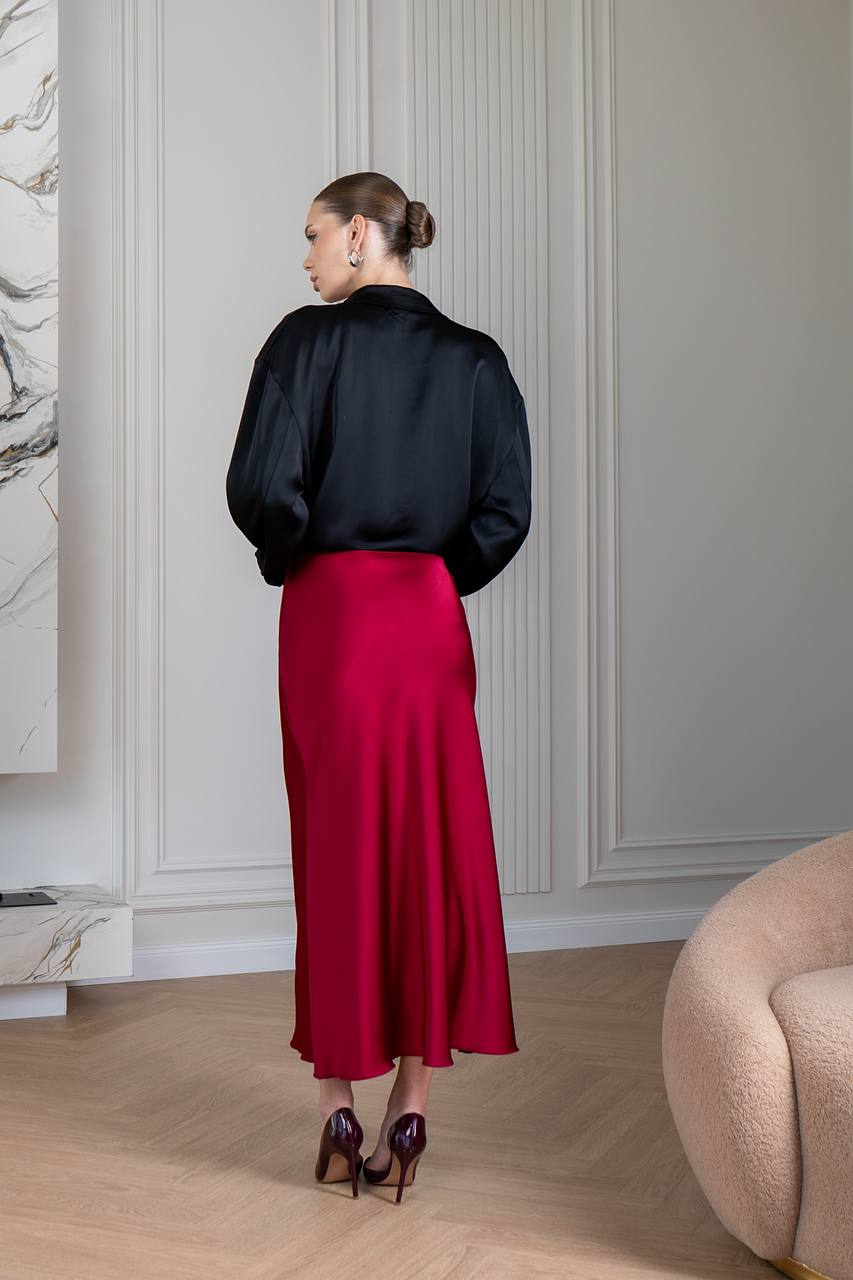 Woman in a black blouse and red skirt standing in a room with light-colored walls and wooden floor.