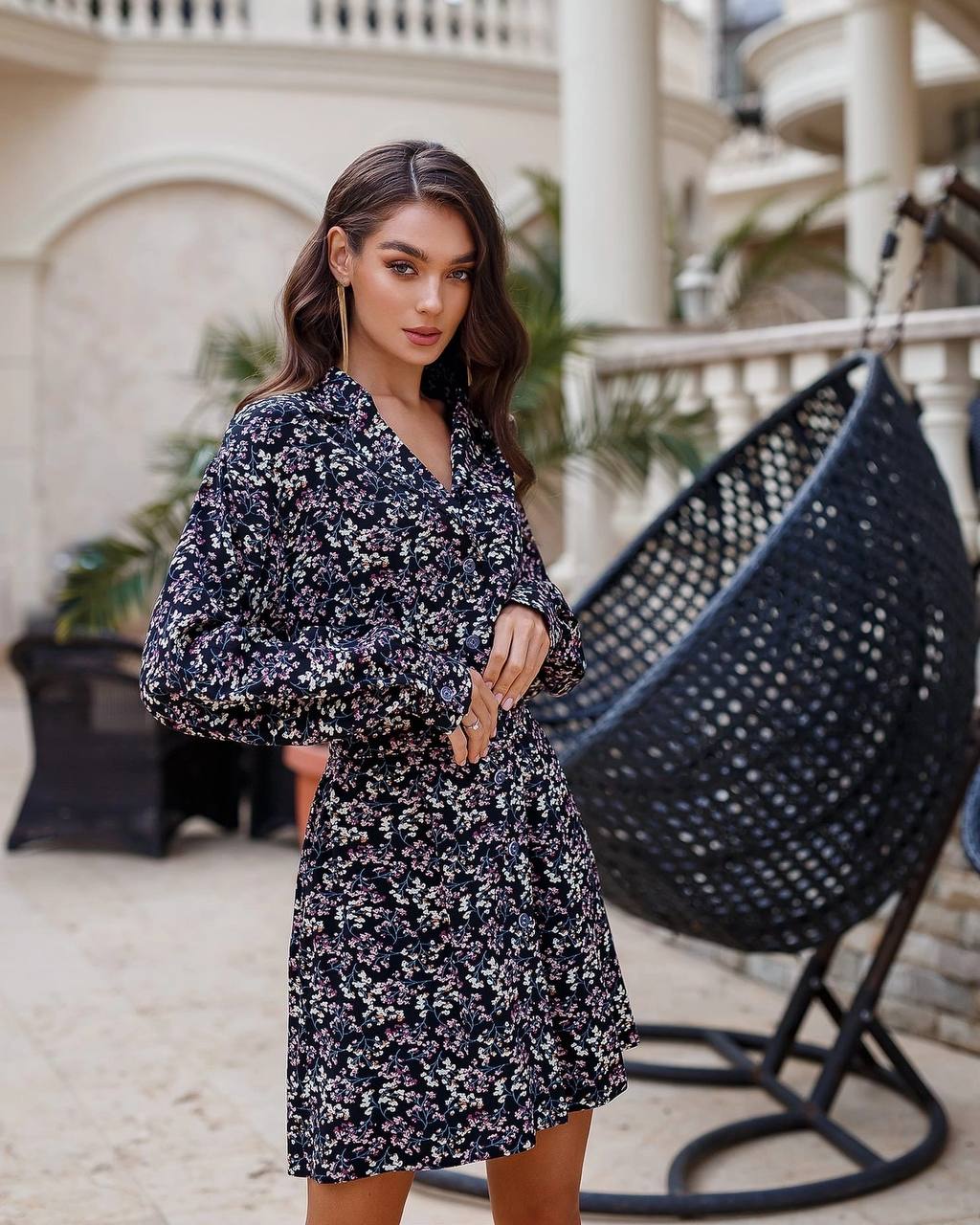 Woman in a floral dress standing in an outdoor setting with a hanging chair.