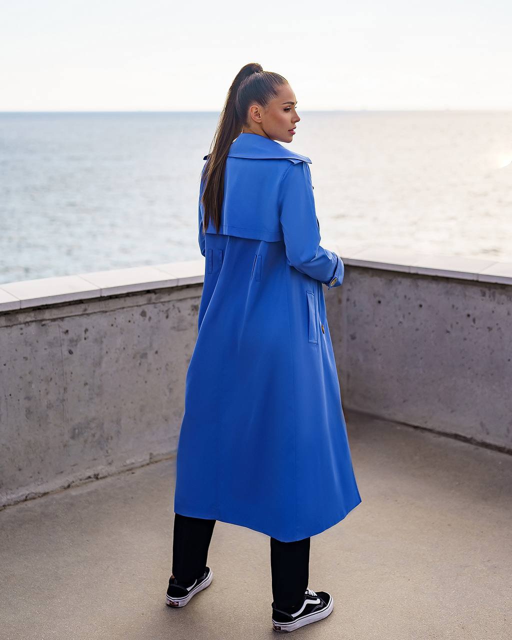 Person wearing a blue trench coat standing by a waterfront.