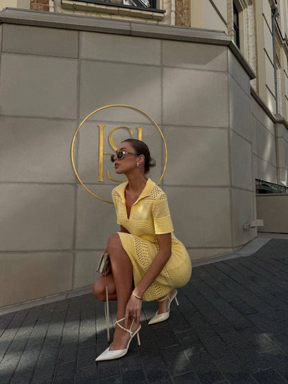 Woman in a yellow dress sitting on a chair in front of a building with a gold logo.