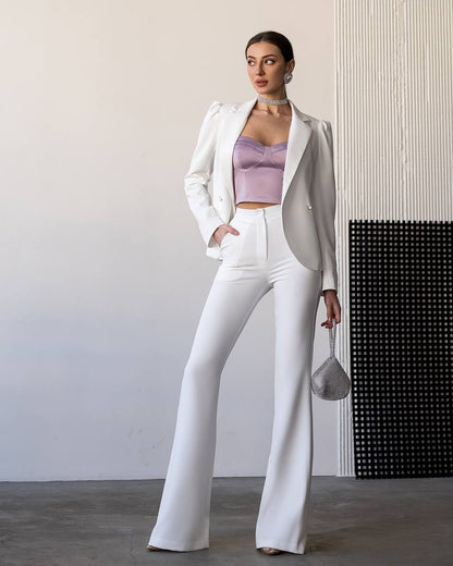 Woman in a white suit with a purple top standing against a neutral wall.
