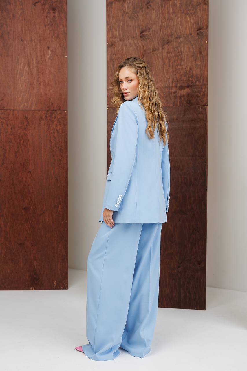 Woman wearing a light blue suit standing against a wooden wall.