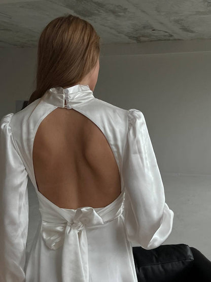 White blouse with open back worn by a person against a plain background
