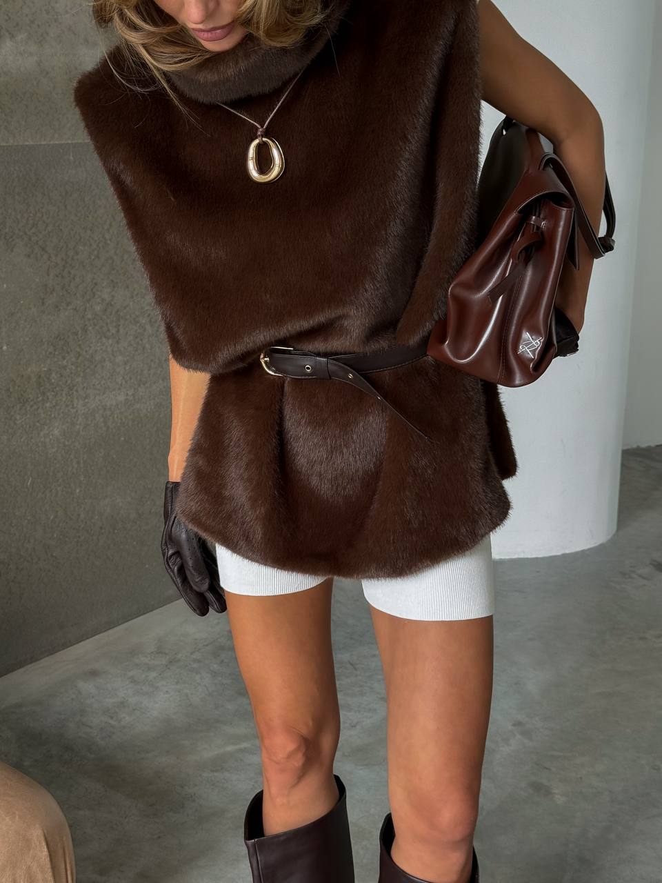 Person wearing a brown fur vest, white shorts, and black boots indoors.