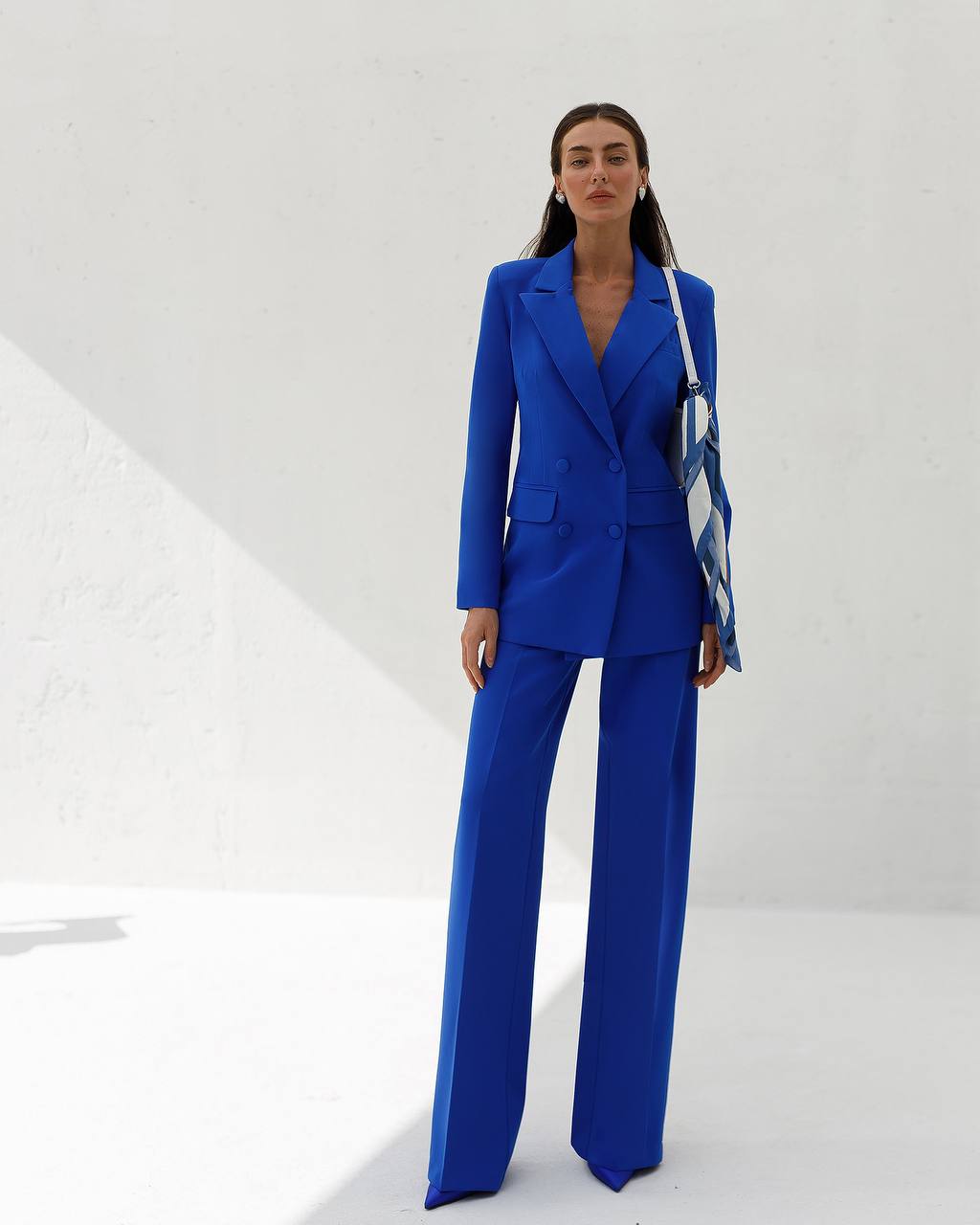 Woman wearing a blue suit holding a striped bag against a white background