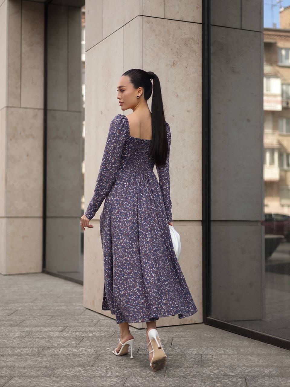 Woman in a long floral dress standing against a modern building.