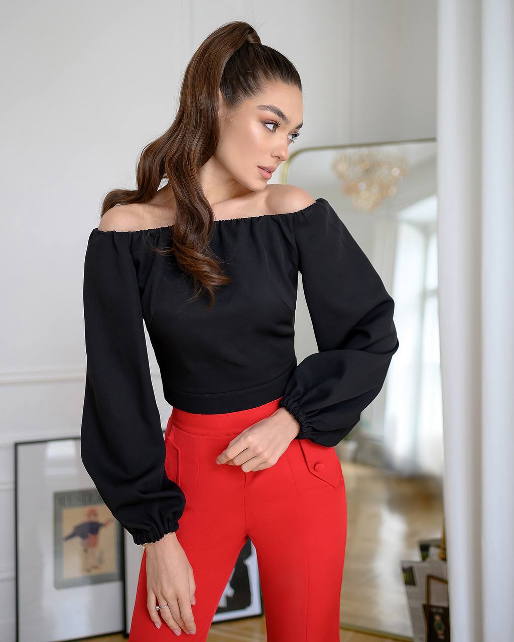 Woman wearing a black off-shoulder top and red pants in an indoor setting.
