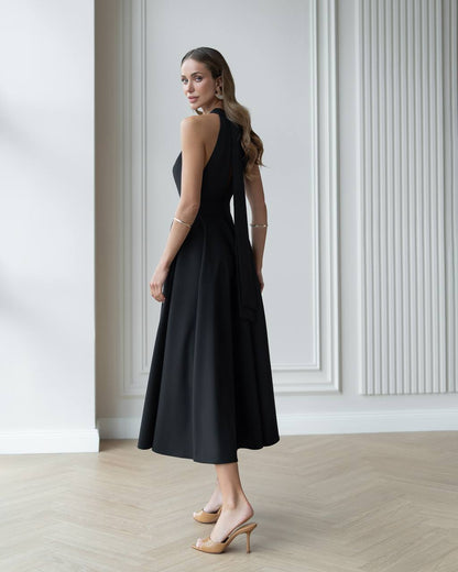 Woman wearing a black dress standing in a room with white walls and wooden flooring.